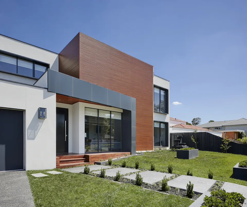 Modern two-storey home with warm interior light and planted surroundings